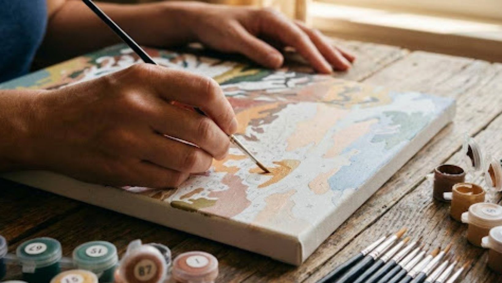 A beginner following the numbered sections on a canvas using acrylic paints from a starter kit